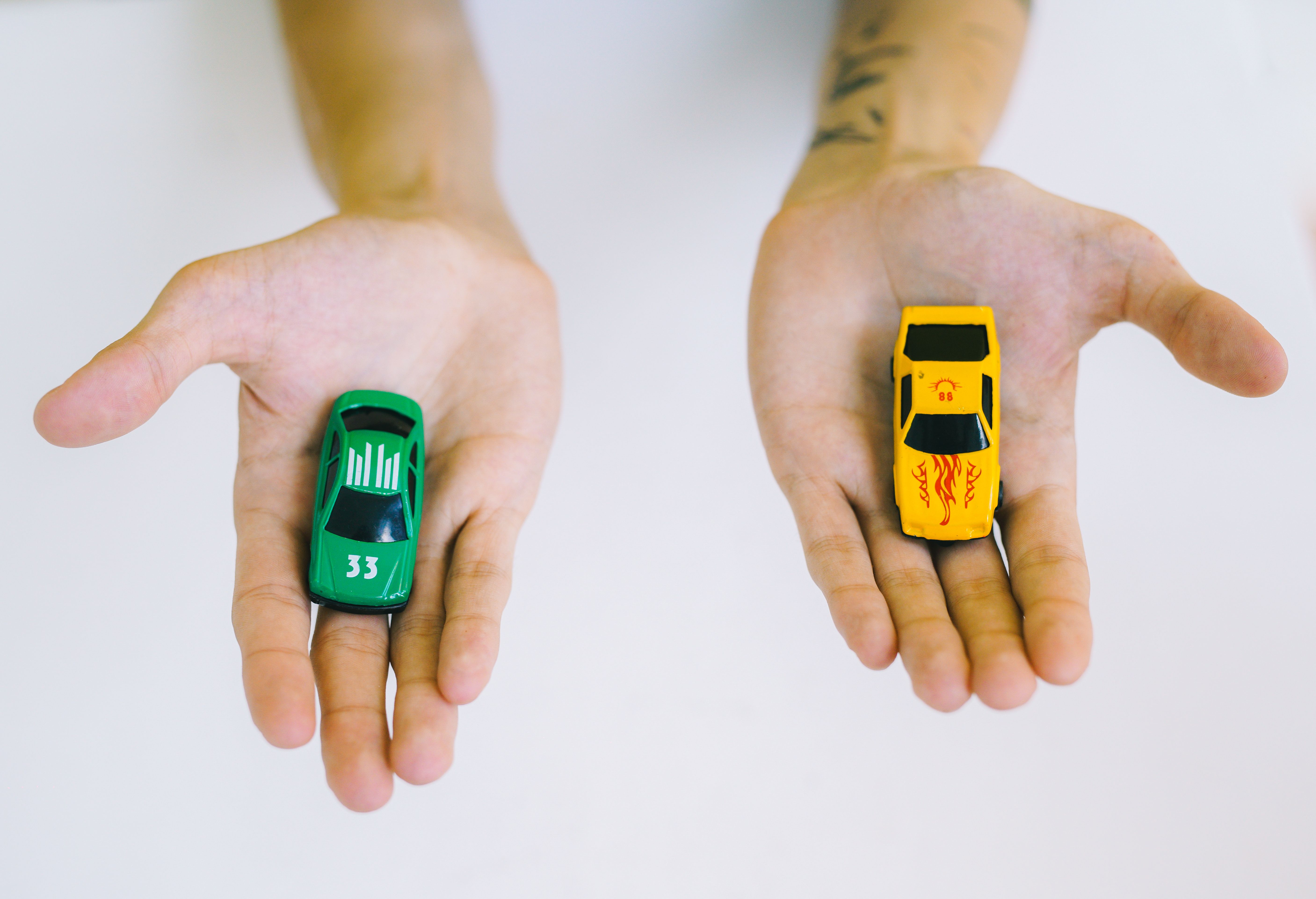 Duas mãos comparando dois carrinhos de brinquedo, representando a escolha entre carro novo e usado